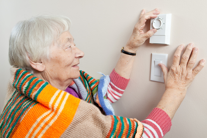 Older person adjusting the thermostat to save money.